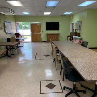 A well-lit meeting room featuring multiple tables and chairs, with green walls and a television on display.