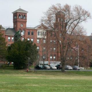 A historic brick building with a tower surrounded by trees and a parking lot.