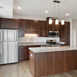 A modern kitchen with wood cabinets, stainless steel appliances, and a central island with pendant lighting.