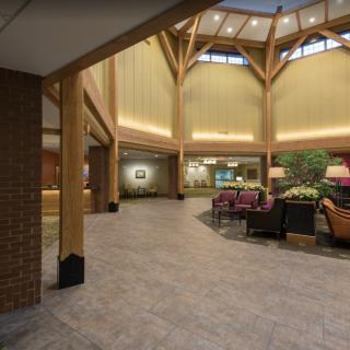 A spacious lobby with wooden beams and cozy seating arrangements, illuminated by natural light.