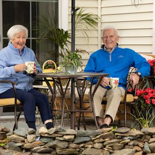 An elderly couple enjoys their time together in a serene outdoor setting, sipping tea by the garden.