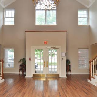 A spacious lobby with a chandelier, featuring wood flooring and large windows.