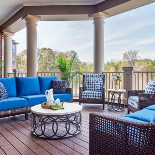 A stylish outdoor patio with blue cushioned furniture and a round table, set against a backdrop of lush greenery.