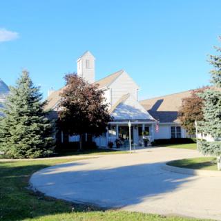 A church building surrounded by trees with a driveway leading to its entrance.