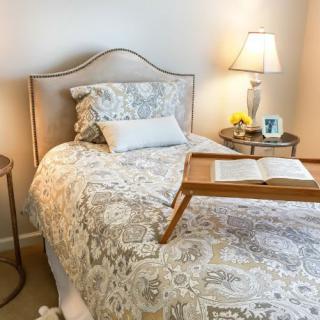 A cozy bedroom setup with a patterned bedspread, bedside lamp, and a book on a tray.