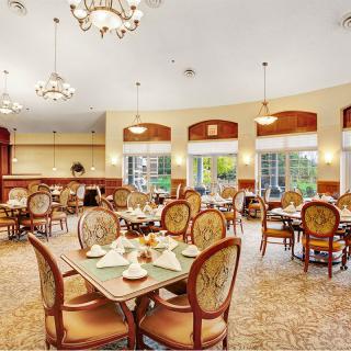 An elegant dining room with ornate chandeliers, set for guests, featuring natural lighting and cozy decor.