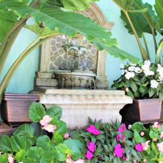 A decorative garden fountain surrounded by lush tropical plants and vibrant flowers.