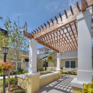 A sunny outdoor space featuring a wooden pergola and lush garden surroundings.