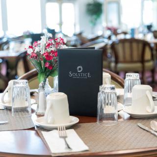 A neatly set dining table with a menu, glasses, cups, and fresh flowers.