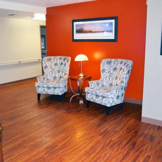 A cozy seating area with two patterned chairs, a lamp, and artwork on an orange wall.