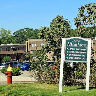 View of an apartment complex with a sign displaying unit numbers and surrounded by greenery.