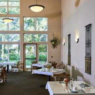 A cozy restaurant interior with several dining tables and large windows providing a view of greenery outside.
