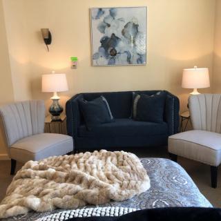 A cozy living room with a dark blue sofa, two armchairs, lamps, and abstract wall art.
