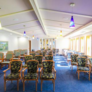 A brightly lit conference room with rows of patterned chairs and large windows.