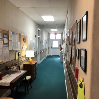 A well-lit hallway with a desk and lamp on one side, adorned with framed pictures and various decorations.