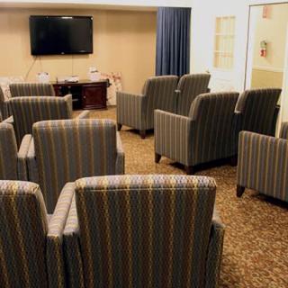 A conference room with multiple upholstered chairs facing a television on the wall.