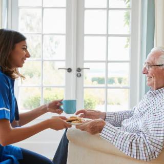 Caregiver offering a drink to an elderly man in a comfortable home setting.