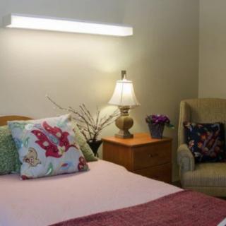 A cozy bedroom with decorative pillows, a side lamp, and an armchair.