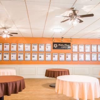An inviting event space featuring neatly arranged tables and an orange accent wall adorned with framed displays.