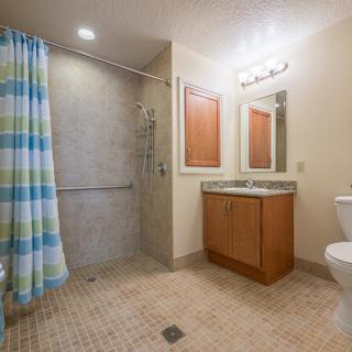 A modern bathroom featuring a shower with a colorful curtain, a vanity with a sink and mirror, and a toilet on tiled flooring.