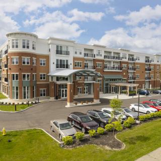 A modern apartment building with a landscaped entrance and parking lot.