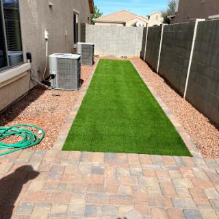 A neatly landscaped backyard featuring artificial grass bordered by paver stones and surrounded by walls.