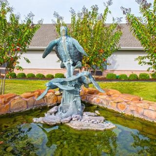 A beautiful fountain sculpture in a garden setting with surrounding trees and landscaping.