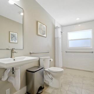 A modern bathroom with a sink, toilet, and large mirror, featuring minimalist decor.