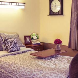 A cozy bedroom with a neatly made bed, decorative pillows, and a nightstand adorned with flowers and a clock.
