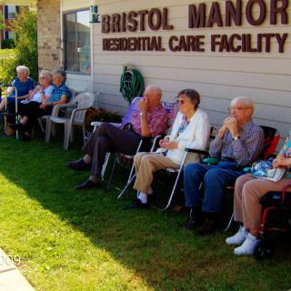 A group of elderly individuals sitting outside a residential care facility.