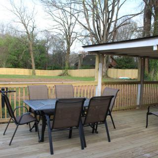 A cozy outdoor patio with a table and chairs, surrounded by a wooden fence and trees.