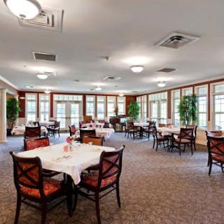 A spacious dining room with neatly arranged tables and chairs, well-lit by ceiling lights and surrounded by large windows.