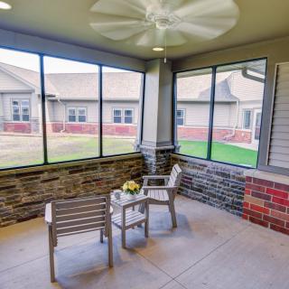 A cozy screened porch with a ceiling fan, featuring two chairs and a small table.