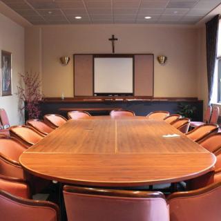 A conference room with a large meeting table, surrounded by chairs and featuring a projector screen and decorative elements.