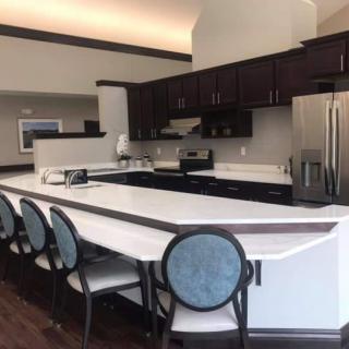 A modern kitchen with a sleek countertop and bar stools, featuring dark cabinets and stainless steel appliances.
