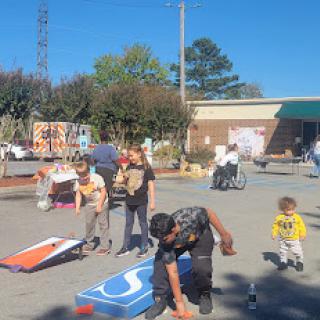 A lively outdoor event where children and adults enjoy playing cornhole together under a clear blue sky.
