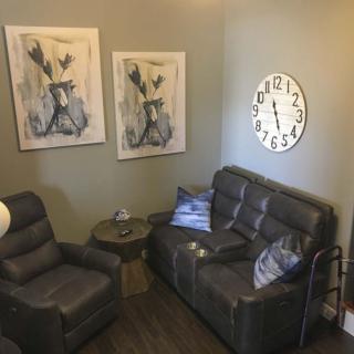 A cozy living room with a comfortable sofa, armchair, wall clock, and abstract artwork.