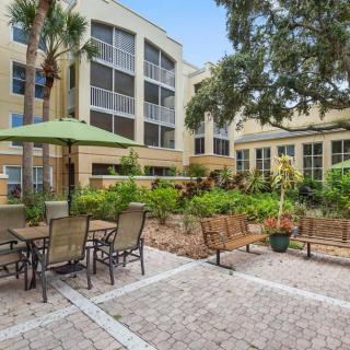 A well-maintained outdoor patio with tables, chairs, and garden beds, adjacent to a residential building.