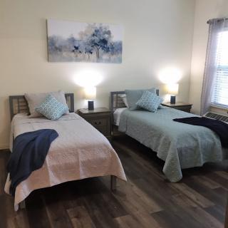 A cozy bedroom featuring two twin beds with complementary bedding, illuminated by bedside lamps and adorned with wall art.
