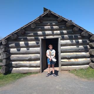 A person standing in the doorway of a log cabin under a clear blue sky.