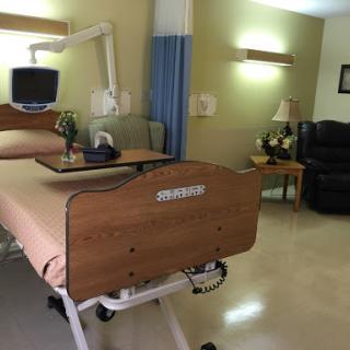A well-equipped hospital patient room with a bed, TV, and seating area.