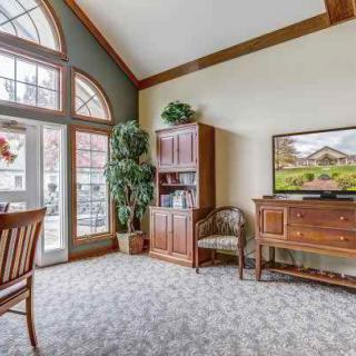 A cozy living room with large windows, a wooden bookshelf, and a television.