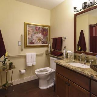 A cozy bathroom with a granite countertop, wall art, and red towel accents.