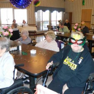 A group of seniors gathered indoors, some in wheelchairs and wearing decorative masks.