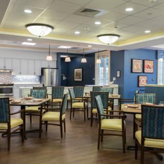 A cozy dining area with neatly arranged tables and chairs, featuring warm lighting and decorative wall art.