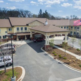 A two-story building with a driveway and parked cars, surrounded by landscaped grounds under a partly cloudy sky.