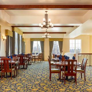 An elegant dining room with neatly arranged tables and chairs, warm lighting, and large windows.