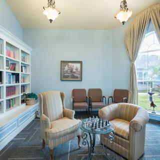 A cozy library room with armchairs, a chess table, and a large window.