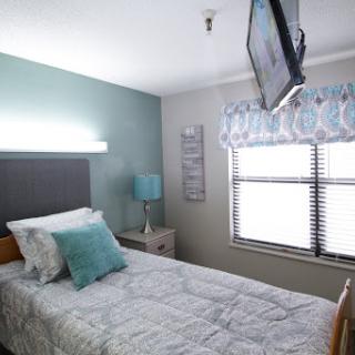 A cozy and modern bedroom featuring a single bed, television, and natural light from the window.