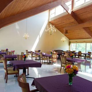A bright and airy restaurant dining area with purple tablecloths and floral centerpieces.